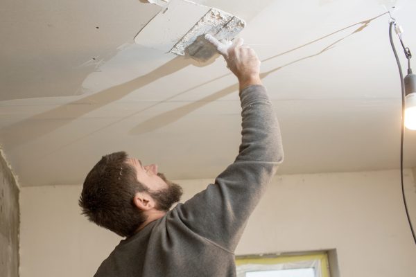 a man with a beard plasterer plasters the ceiling in a room with a spatula