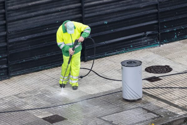 Worker cleaning a sidewalk with high pressure water jet machine. Copy space